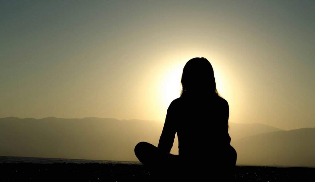 Femme en train de méditer devant le coucher de soleil.