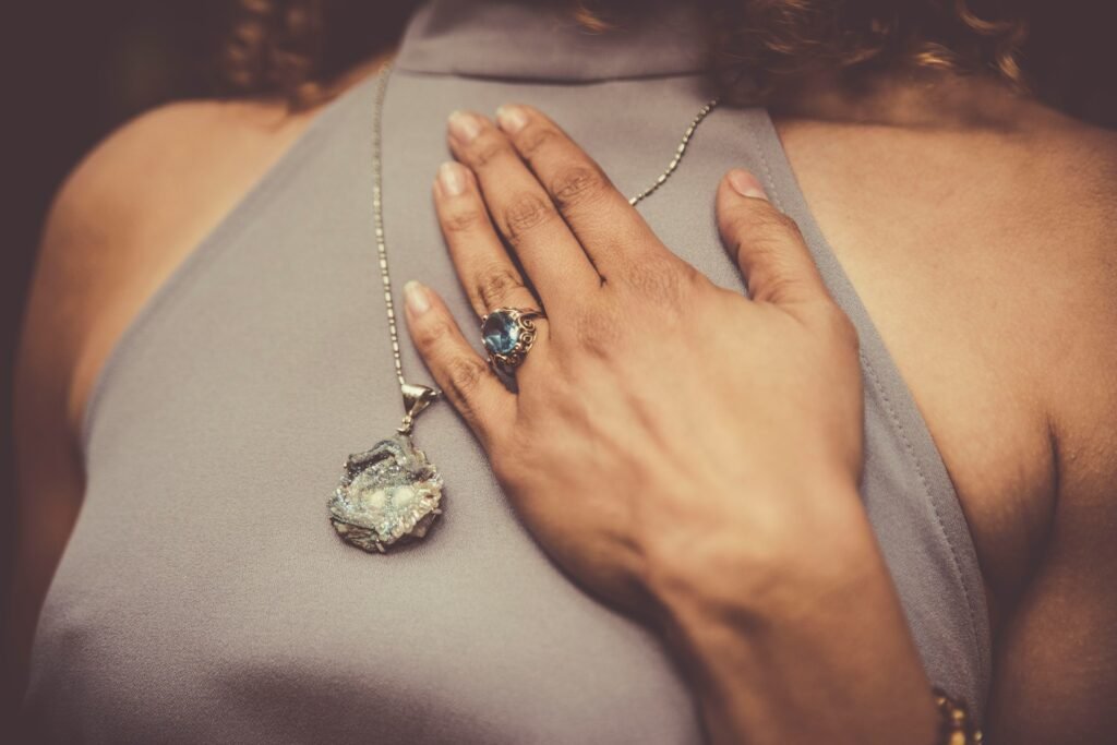 Femme qui a sa main sur sa poitrine. Porte une bague et un pendentif