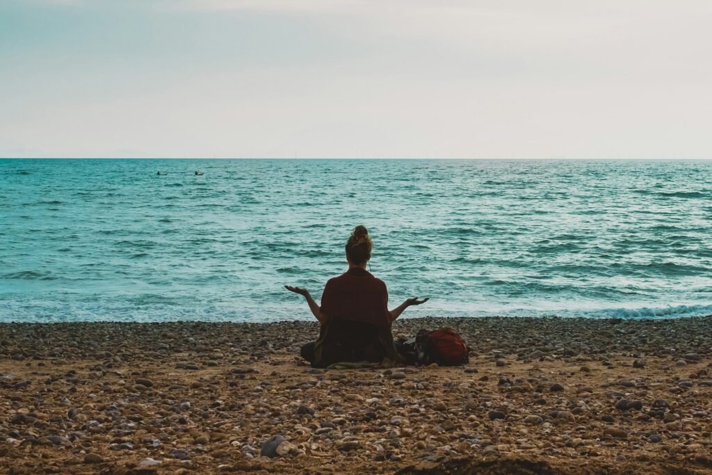 Femme en train de méditer devant la mer sur une plage de galet.