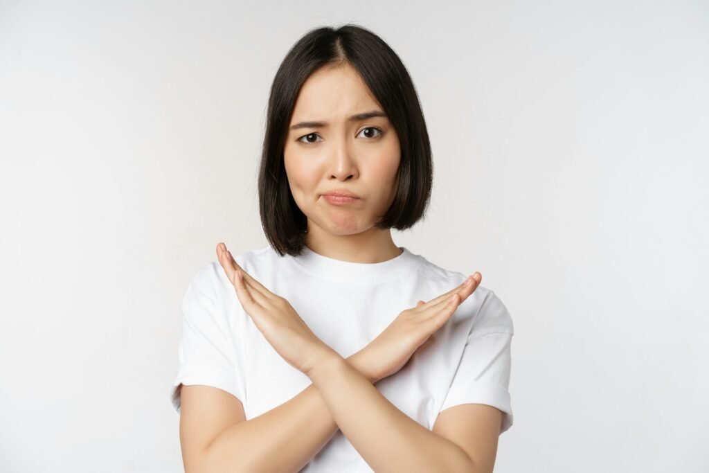 Femme cheveux bruns et t-shirt blanc qui croise les bras en guise de croix.