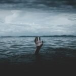Main qui sort de la surface de l'eau dans la mer avec un fond noir.
