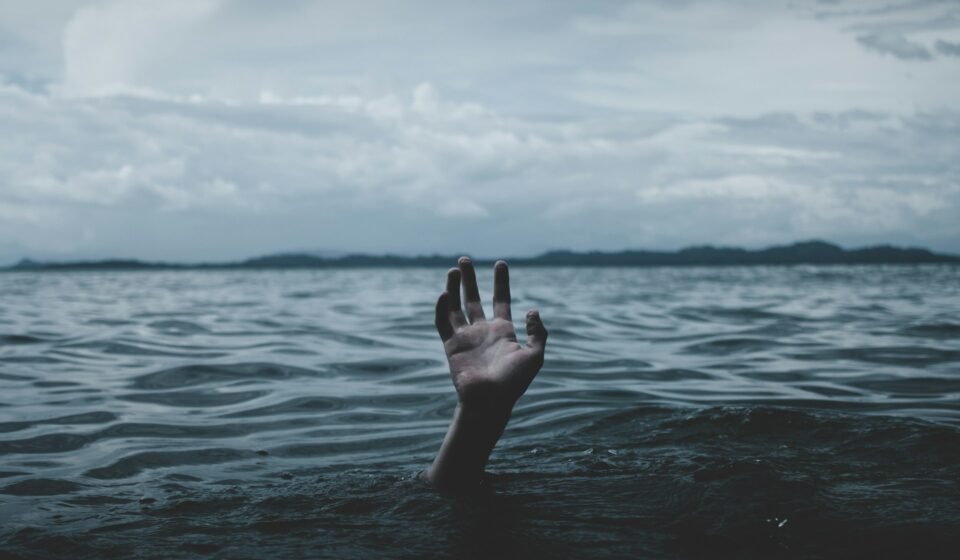 Burn-out : Symptômes et prévention de l’épuisement Main qui sort de la surface de l'eau dans la mer avec un fond noir.