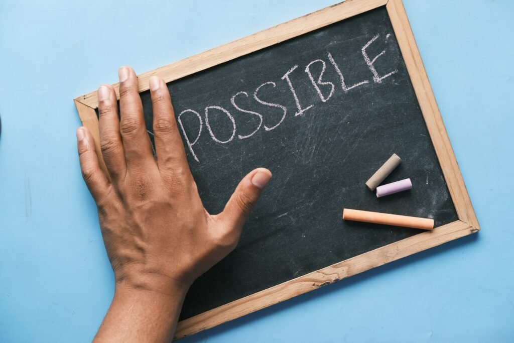 Ardoise avec inscription "possible" avec des craies de couleurs et une main posée dessus.