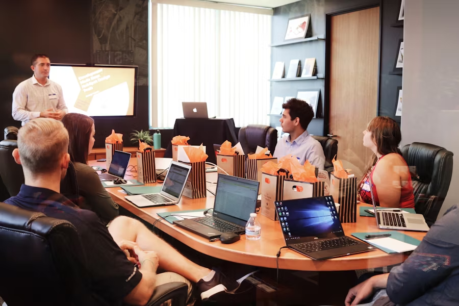Six personnes autour d'une table de travail avec leurs ordinateurs en réunion.