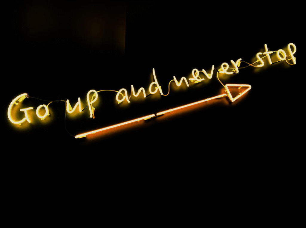 Néon lumineux avec l'inscription 'Go up and never stop' et une flèche pointant vers le haut.
