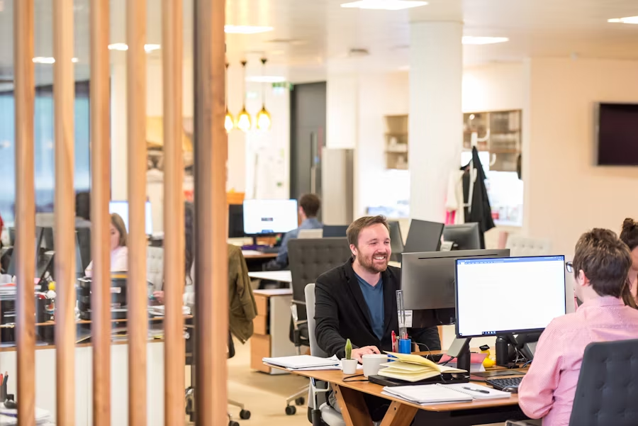Open space où l'on voit des personnes souriantes devant leur bureau